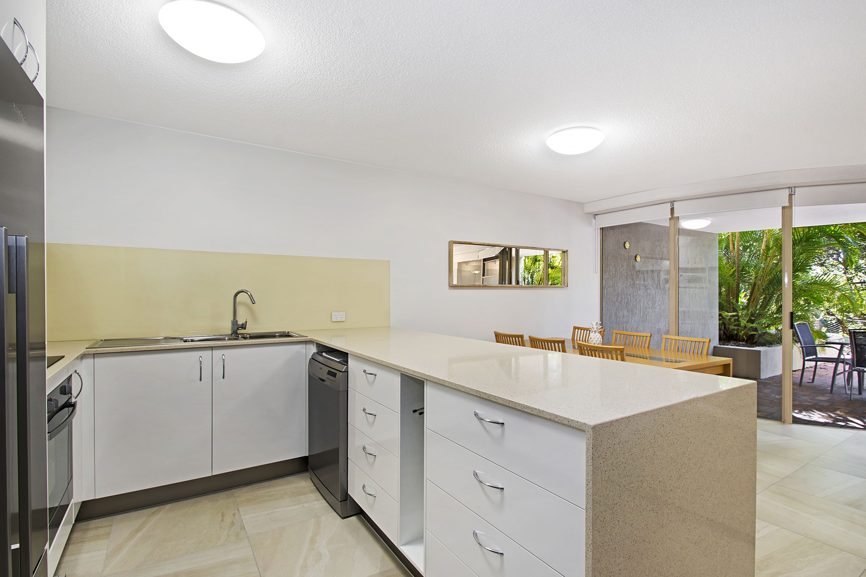 A modern kitchen with white cabinetry, a built-in dishwasher, and a large island with a sink.