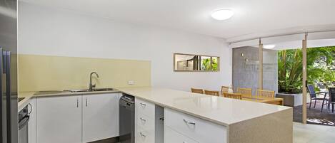 A modern kitchen with white cabinetry, a built-in dishwasher, and a large island with a sink.