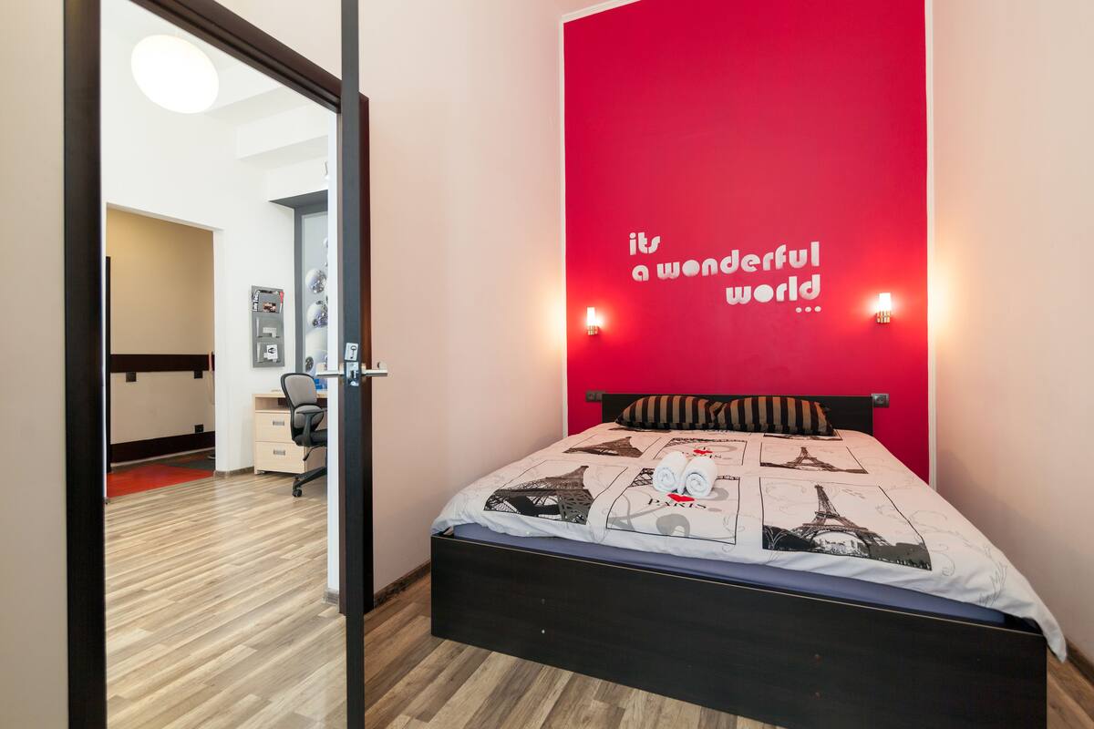 A bedroom with a bed, a red accent wall, and a motivational quote.