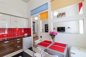 A modern kitchen with white cabinets, a red tiled backsplash, and a dining area with a glass table and chairs.