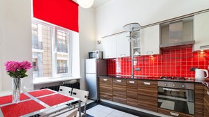 A modern kitchen with a black and white checkered floor, red tiled backsplash, and a dining area with a table set for two. - Modern Properties Lviv (Lviv)