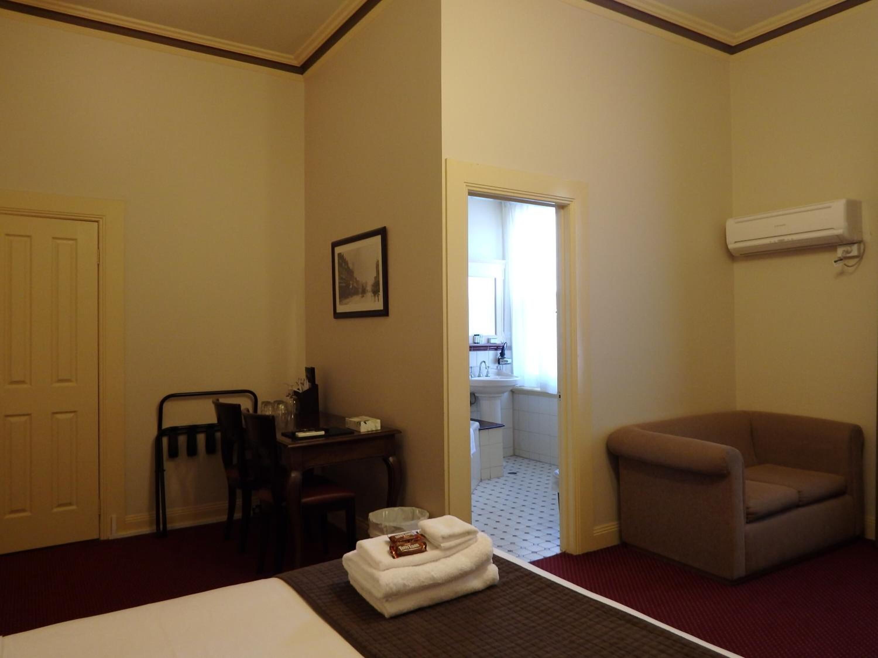 Habitación de hotel con cama, una silla, un escritorio con silla, un cuadro en la pared y un aire acondicionado.