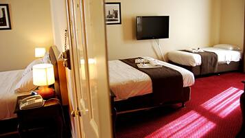 A hotel room with two beds, a TV, a telephone, and a red carpet.