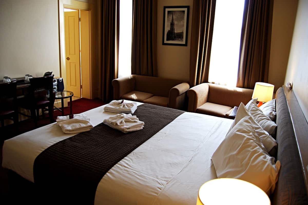 A hotel room with a large bed, two armchairs, a desk with a chair, and a framed picture on the wall.