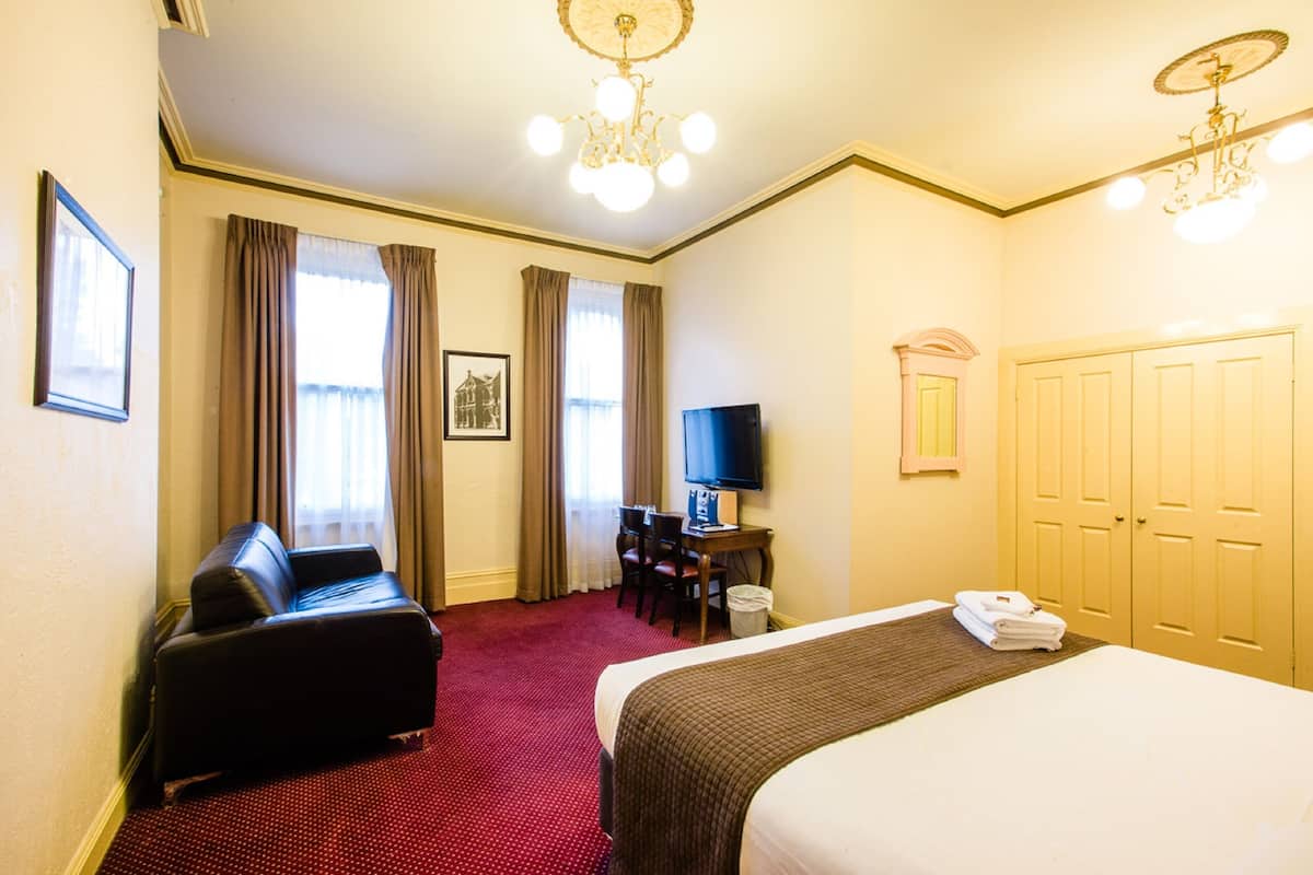 A hotel room with a bed, a desk, a chair, a television, and a wardrobe.