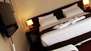 Ett hotellrum med två sängar, båda med vita sängkläder och en brun sänggavel. På väggen sitter en platt-TV och bredvid sängen står ett nattduksbord med en lampa.