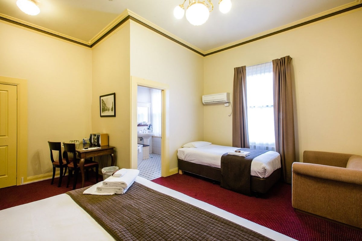 A hotel room with a bed, a desk, a chair, a small table, and a window with curtains.