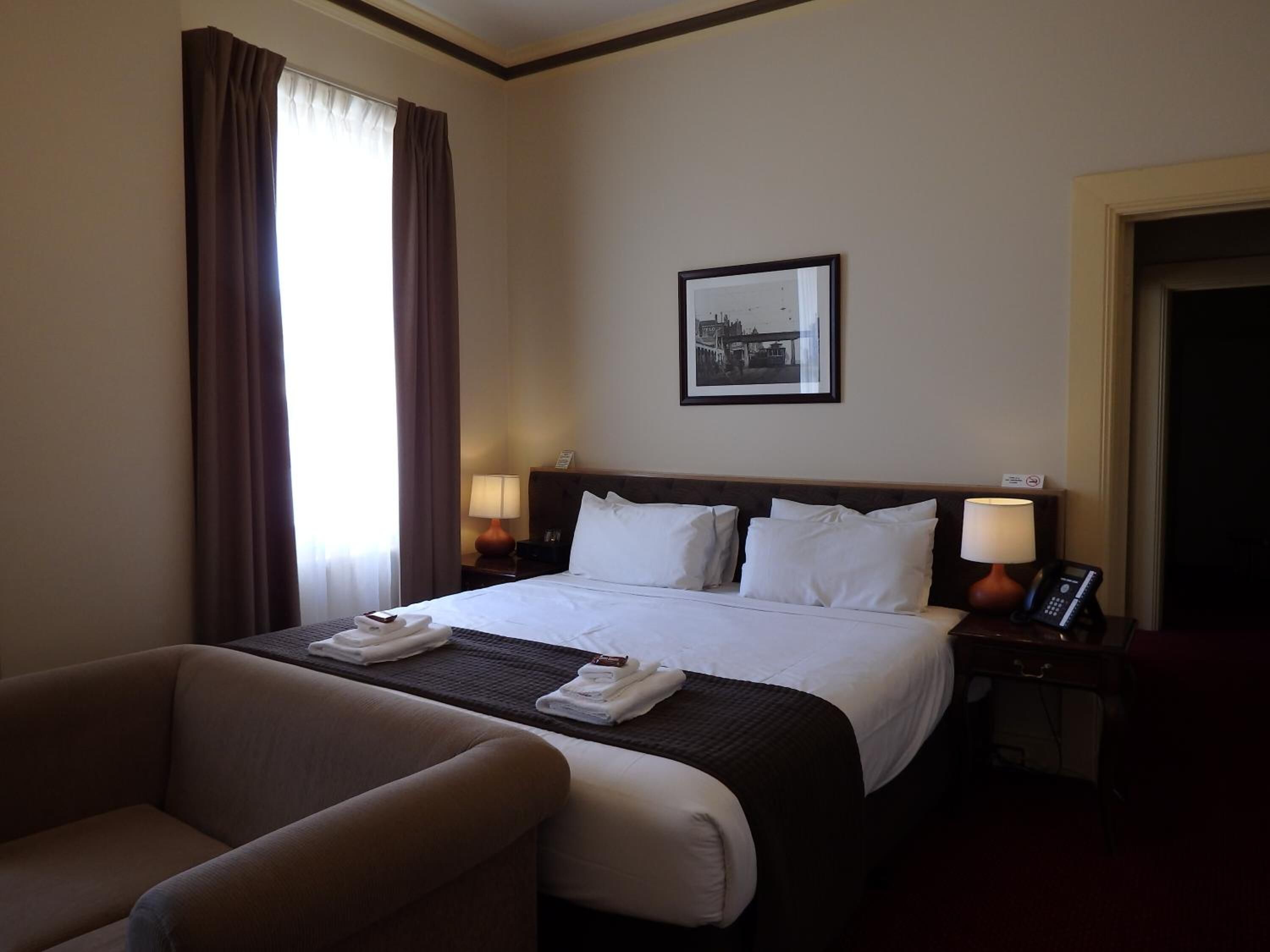 Habitación de hotel con una cama grande, dos lámparas de noche, un cuadro en la pared y una silla.