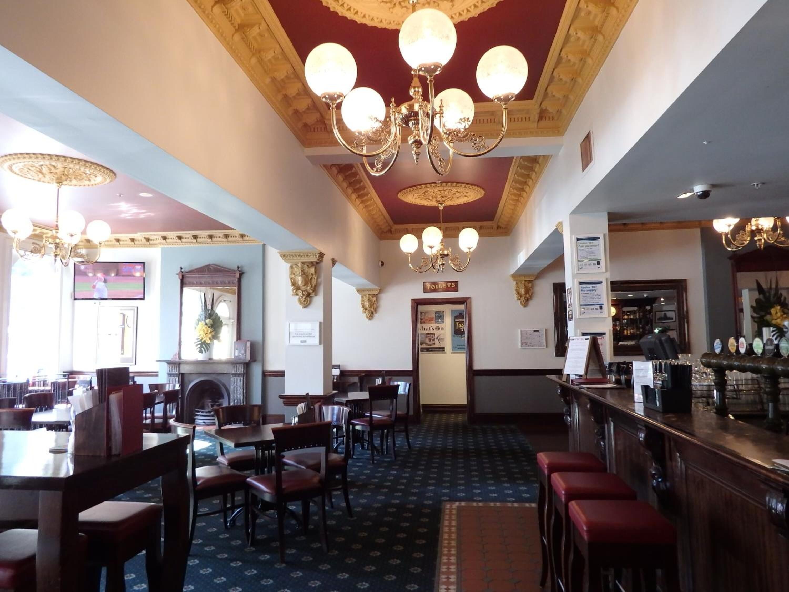 Un restaurante con zona de bar, varios candelabros y alfombra estampada.