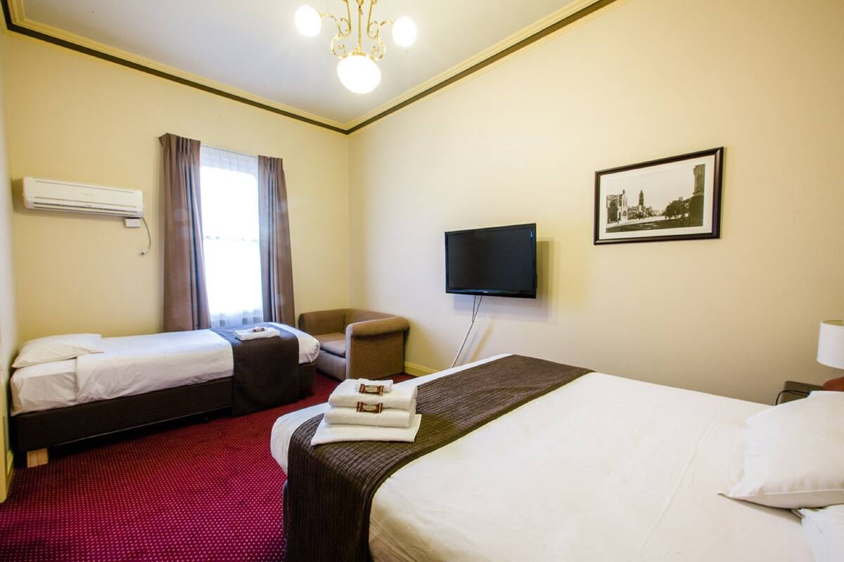 A hotel room with two beds, a television, a picture on the wall, and an air conditioner.