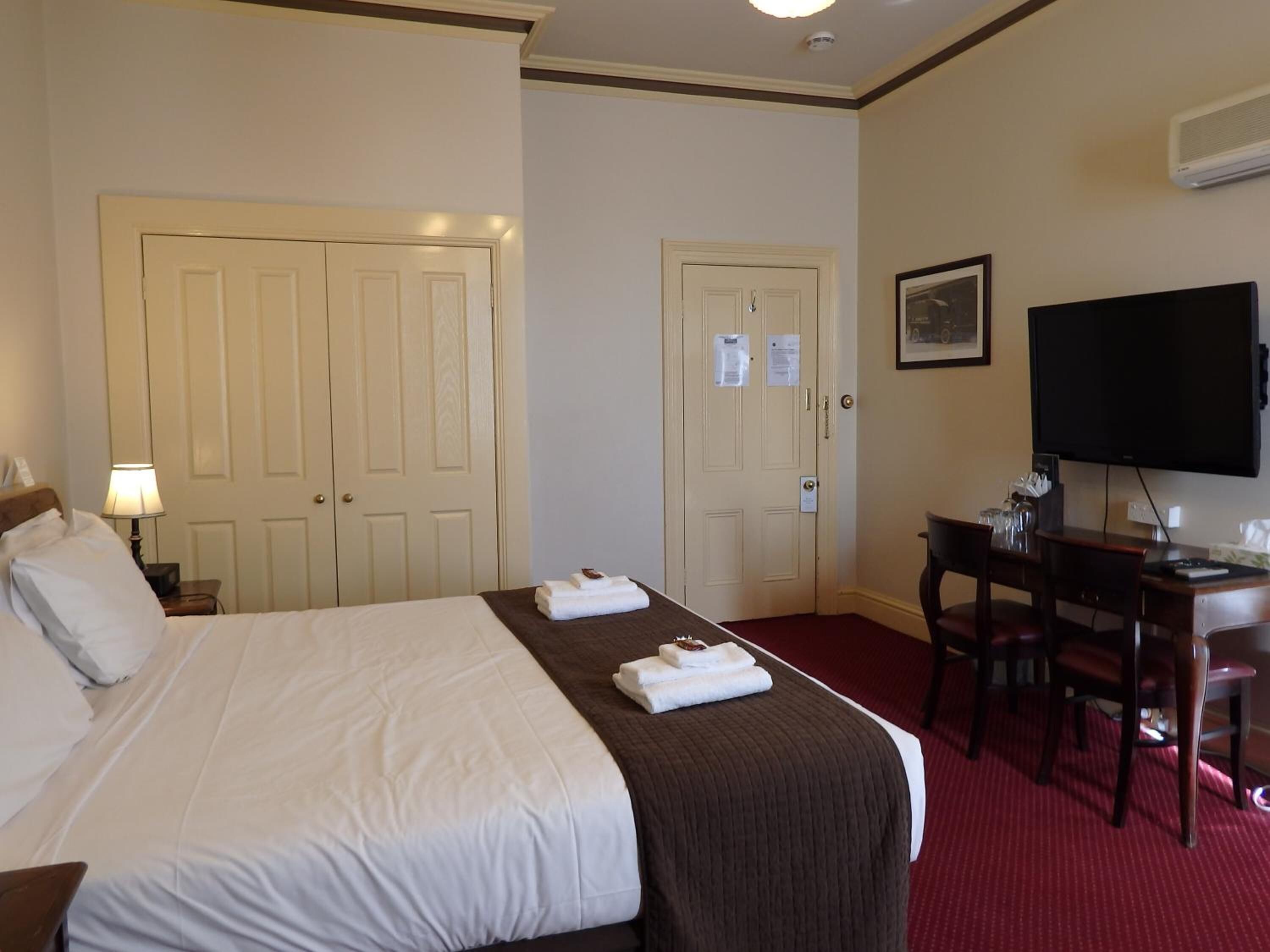 A hotel room with a bed, a desk, a chair, a television, and two doors.