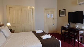 A hotel room with a bed, a desk, a chair, a television, and two doors.