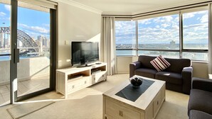 Ein modernes Wohnzimmer mit Fernseher, Sofa und Couchtisch, mit großen Fenstern und Blick auf die Stadt.