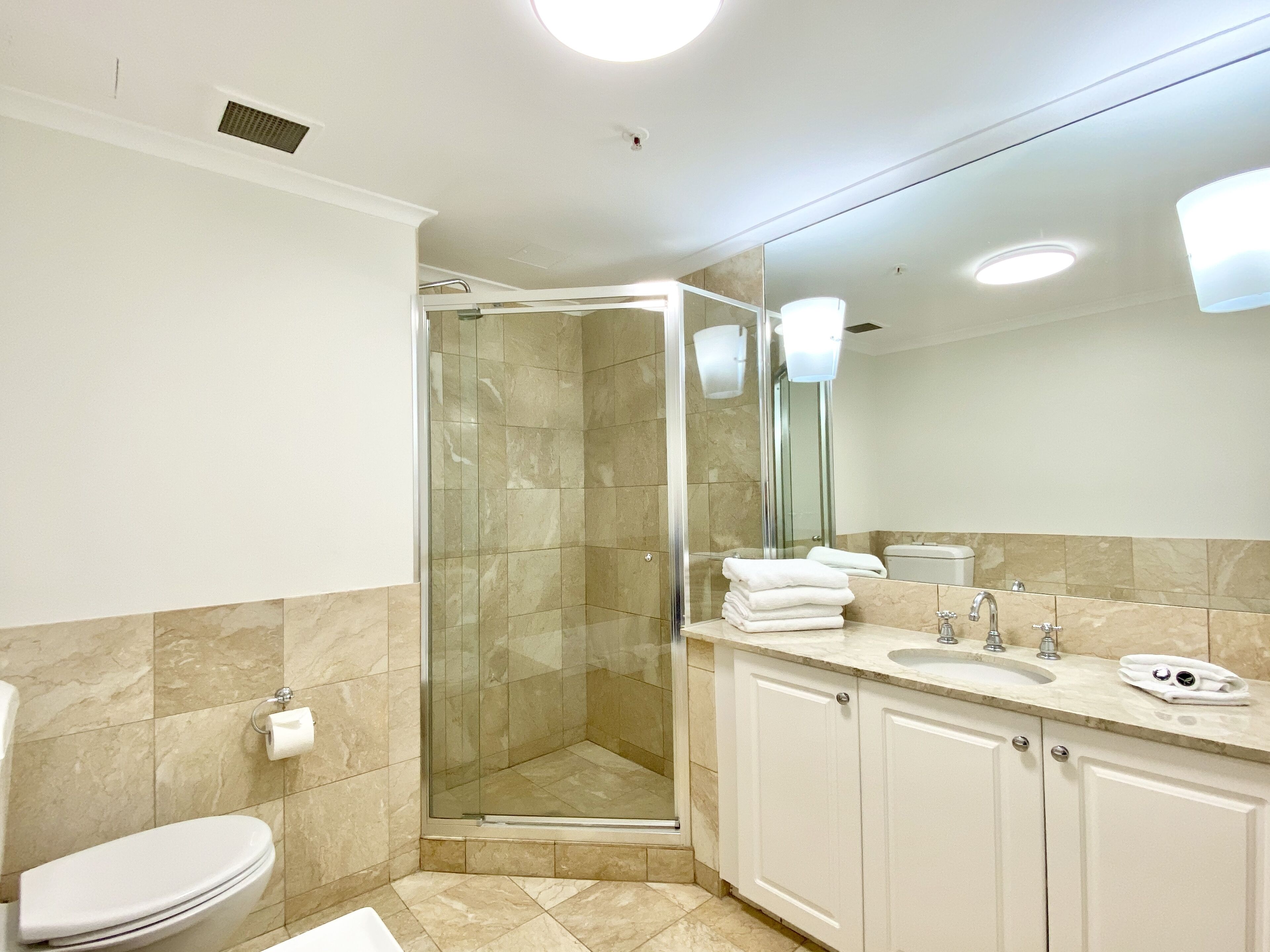 Une salle de bain moderne avec une douche à parois de verre, des toilettes et un lavabo surmonté d’un miroir.