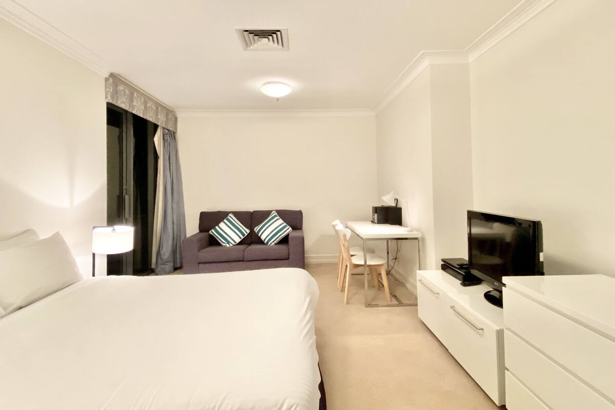 A hotel room with a bed, a desk, a chair, a TV, and a dresser.