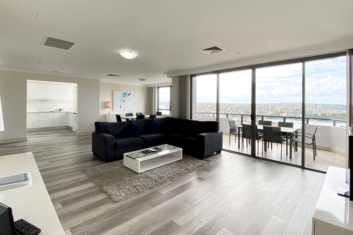 A modern living room with a large window, a sofa, a coffee table, and a dining area with chairs.