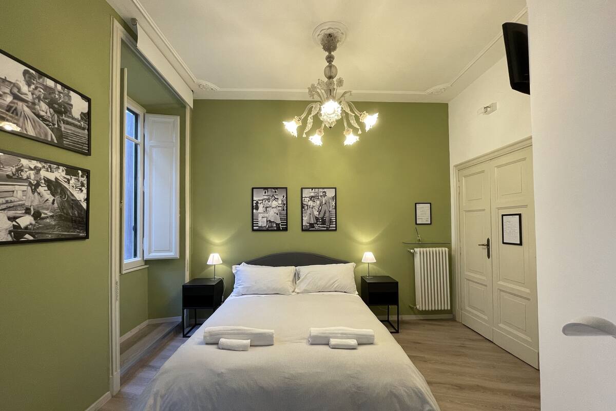 A bedroom with a bed, two bedside lamps, a chandelier, and framed pictures on the wall.