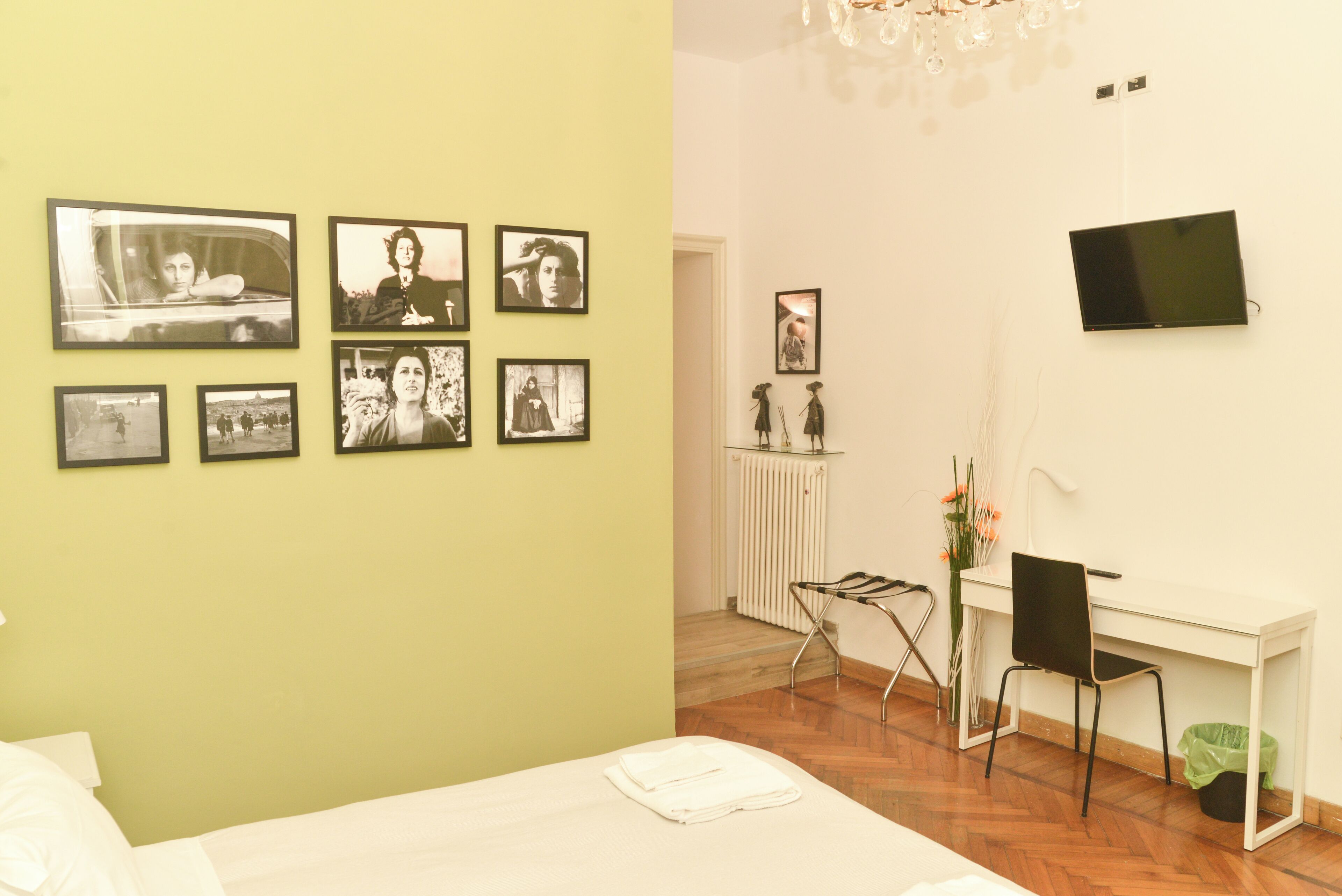 A room with a bed, a desk, a chair, a TV, and several framed pictures on the wall.