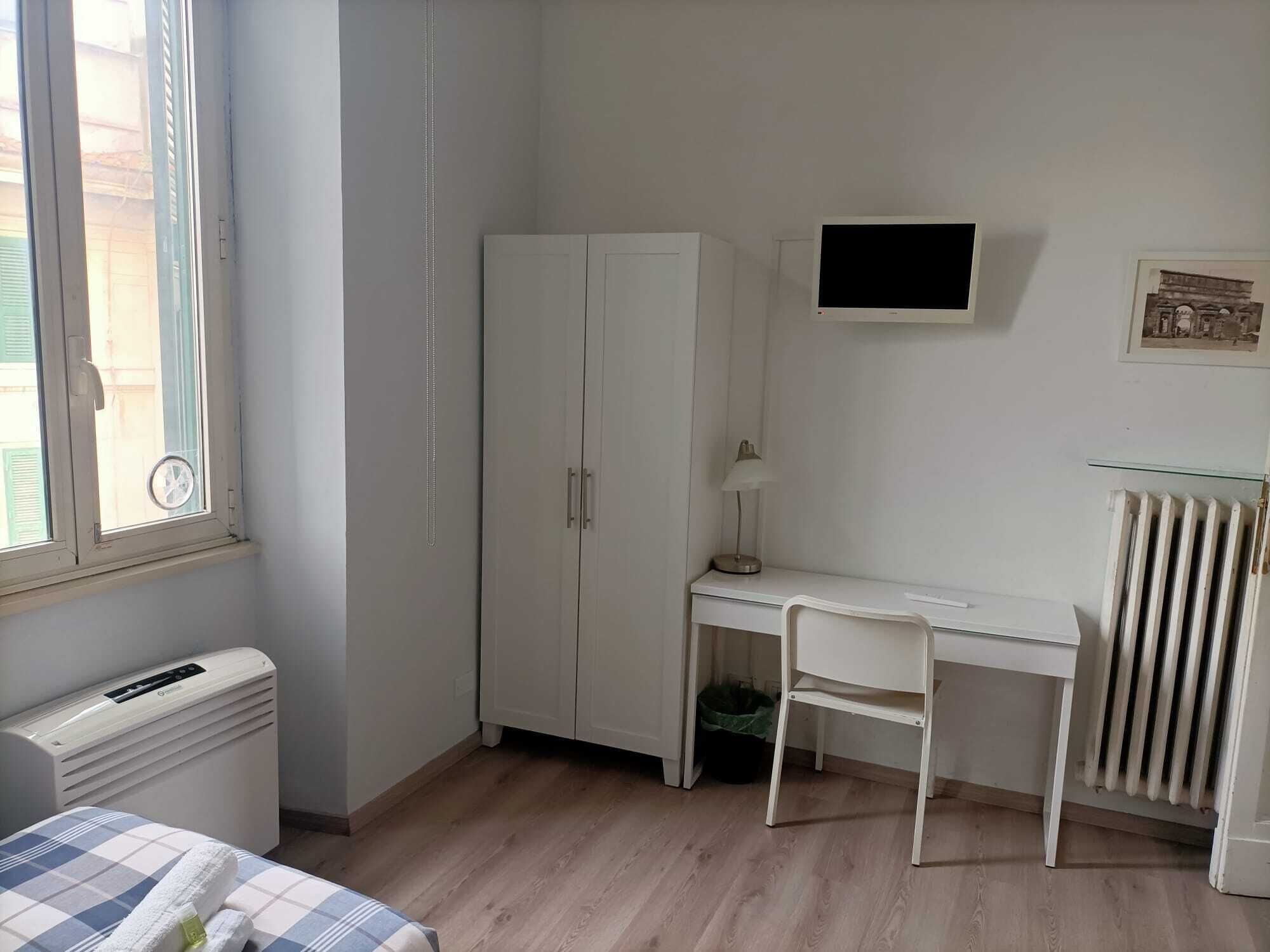 A bedroom with a bed, a desk, a wardrobe, a radiator, and a window.