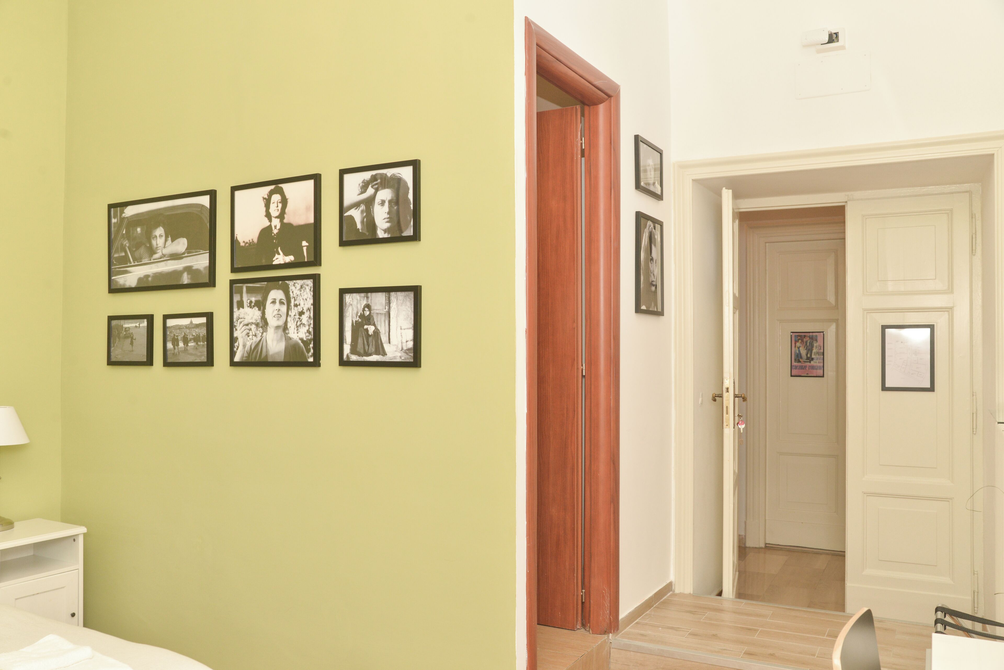 Una habitación con una cama, una mesita de noche y una pared con fotografías enmarcadas.