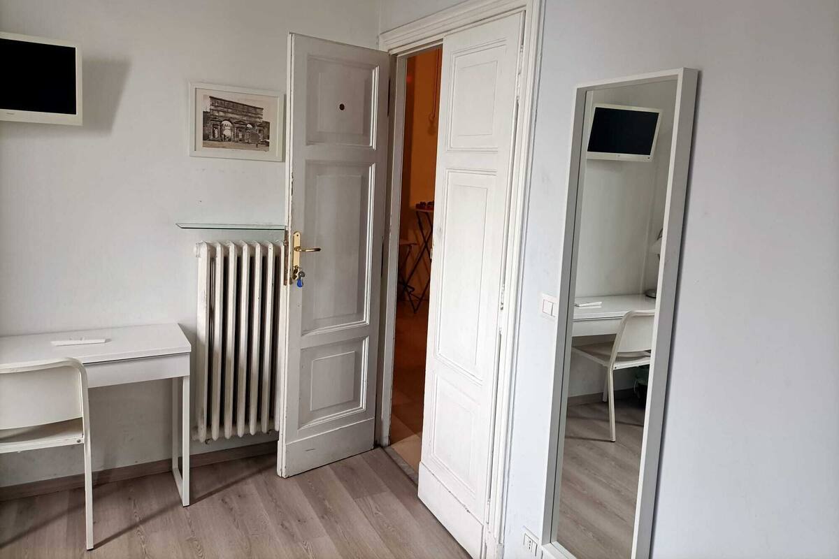 A room with a white desk, a radiator, a door, and a mirror.