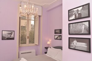 A bedroom with a bed, a chandelier, a window, and four black-and-white photographs on the wall. - Colazione Al Vaticano (Rome)