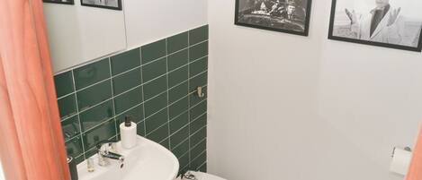 Un baño con lavamanos, inodoro y paredes de azulejos verdes. Hay cuadros enmarcados en la pared.