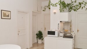 A white kitchen with a microwave, sink, and cabinets. There is a potted plant and a framed picture on the wall. - Colazione Al Vaticano (Rome)