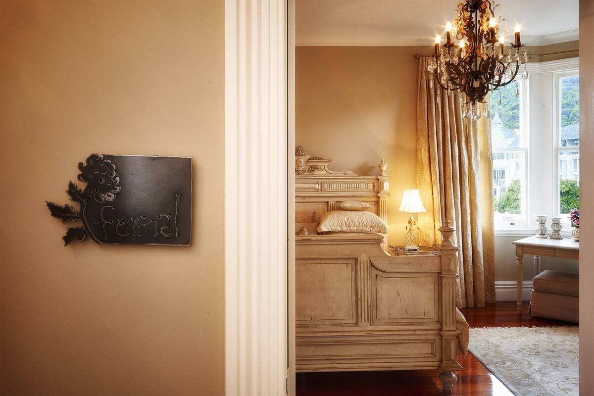 A formal room with a bed, a chandelier, and a view of the outdoors.