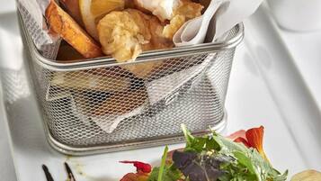 A basket of fried fish and chips with lemon wedges and parsley, accompanied by a plate of mixed greens and strawberries.