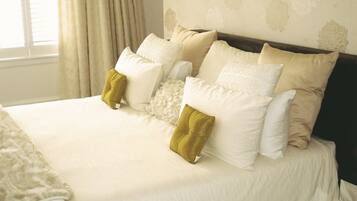 A neatly made bed with multiple pillows and a blanket, a window with curtains, and a wall with a floral pattern.