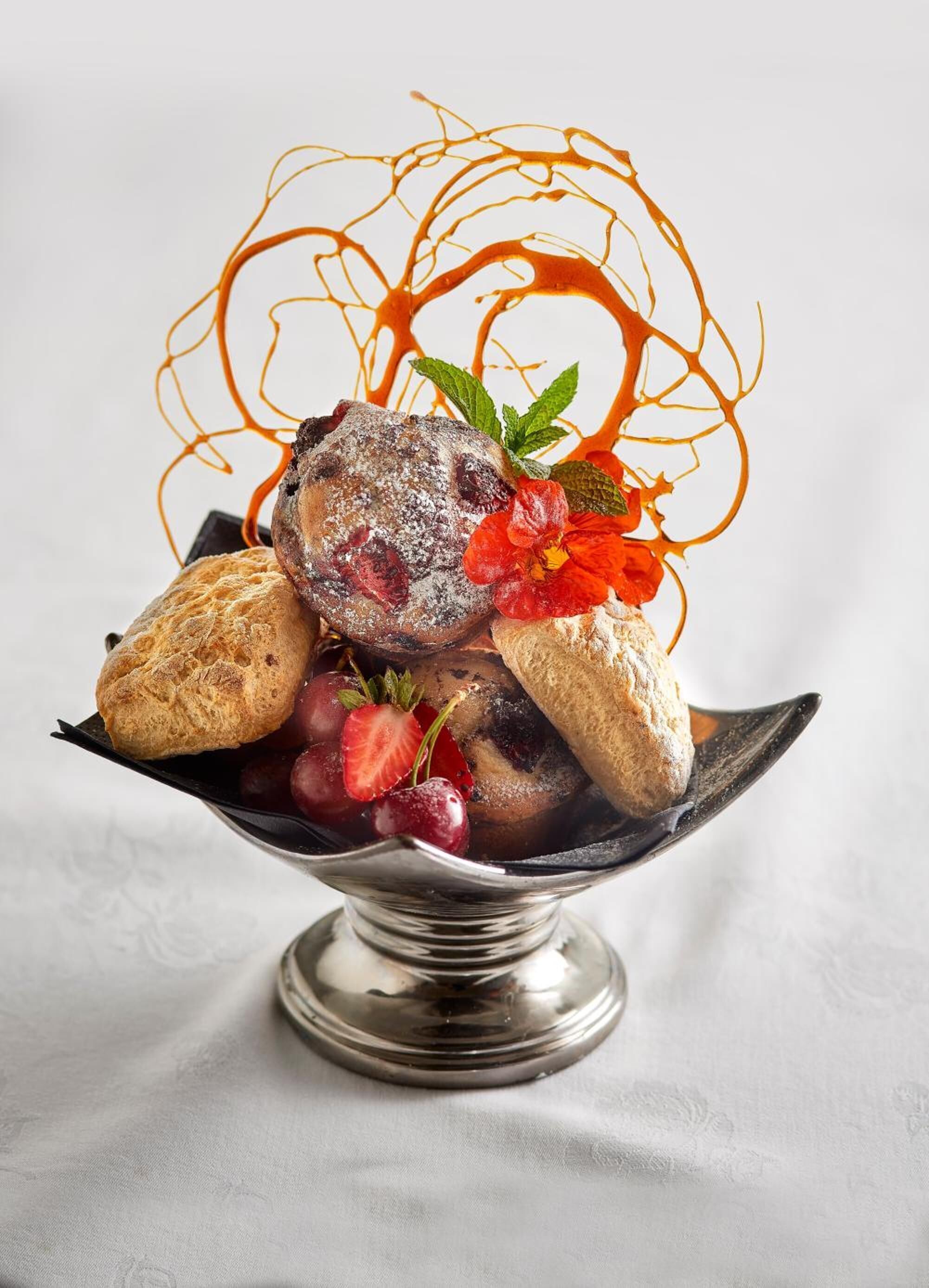 A dessert with a scoop of ice cream, strawberries, and a decorative sauce on a silver serving dish.