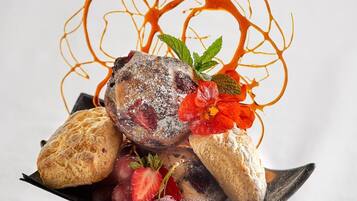 Un postre con una bola de helado, fresas y salsa decorativa sobre un plato de plata.