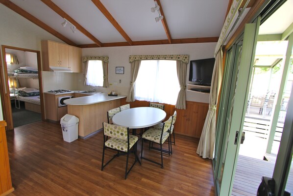A compact kitchen with a dining area, wooden floors, and a view through the open door.