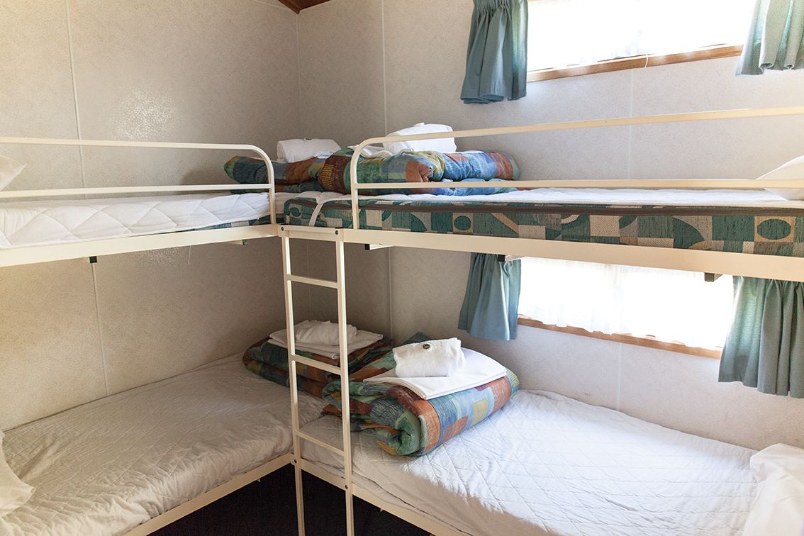 A bunk bed room with a ladder, a window with curtains, and a bed with a quilt.