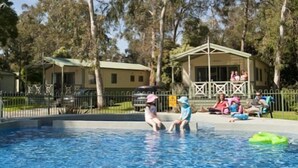 Una piscina con agua azul cristalina rodeada de árboles y un pequeño pabellón.