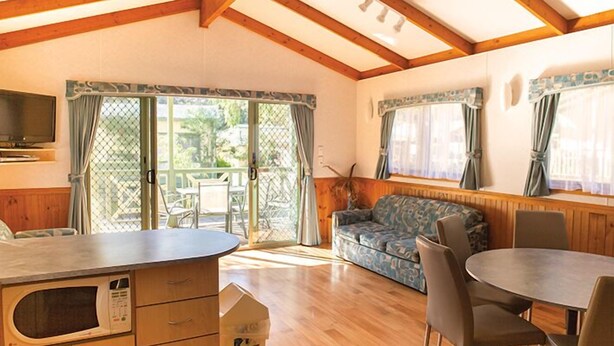 Una habitación acogedora con techo de madera, un sofá, una mesa de comedor con sillas, un microondas y un televisor.