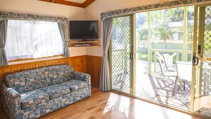 Una habitación acogedora con un sofá estampado, un televisor de pantalla plana y un ventanal corredero que da a un patio exterior con sillas.