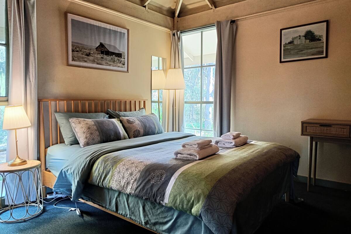 A neatly made bed with a patterned bedspread, a bedside lamp, and a framed picture on the wall.