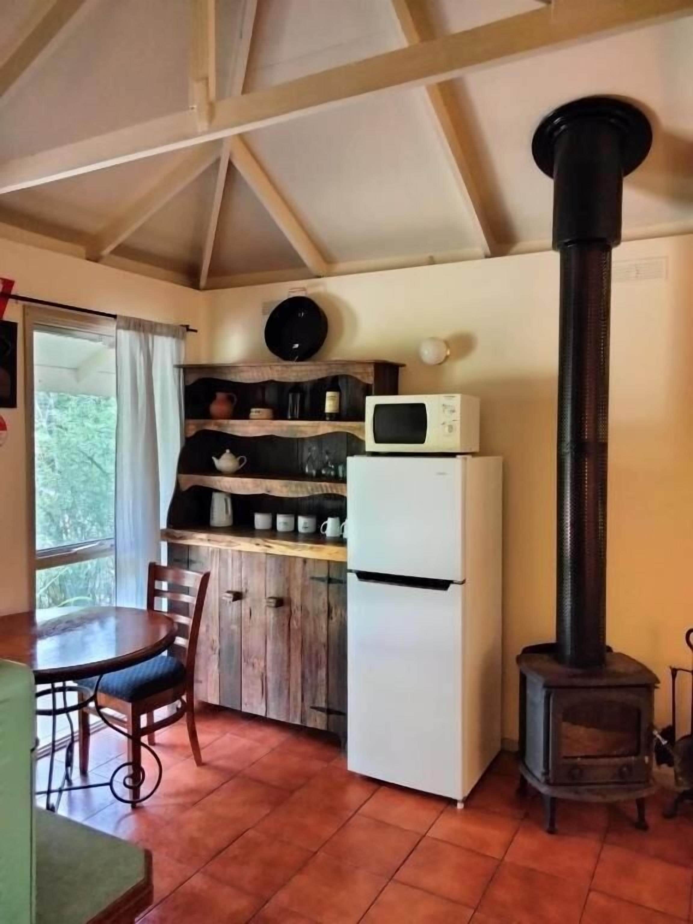 Cocina compacta con una mesa de madera, sillas, un refrigerador, un microondas y un estufa de leña.