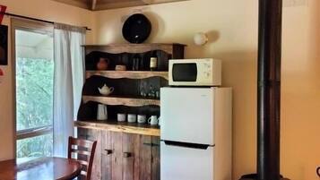 A compact kitchen with a wooden table, chairs, a refrigerator, a microwave, and a wood-burning stove.