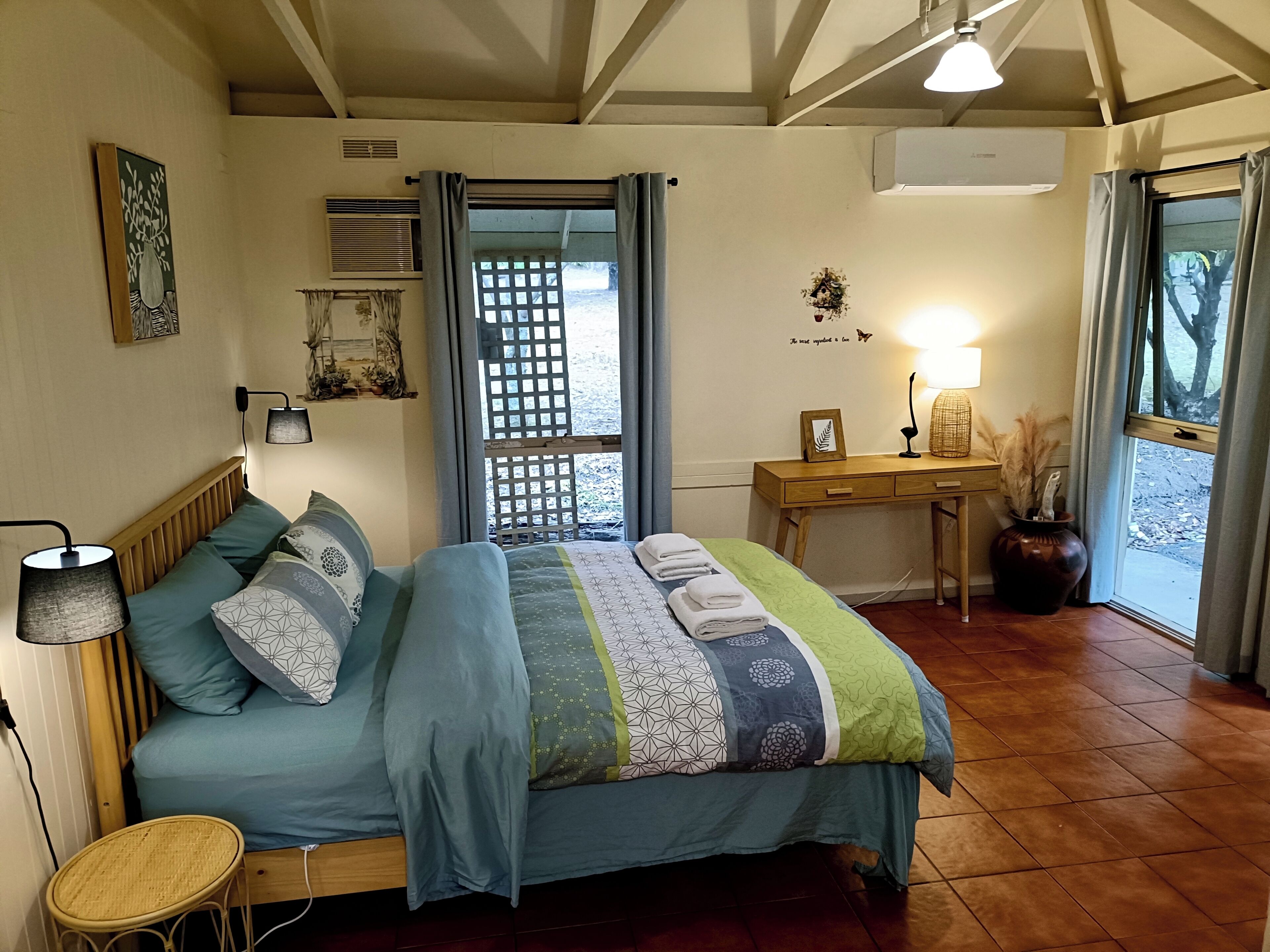 Een slaapkamer met een bed, nachtkastje, lamp en een bureau met stoel.