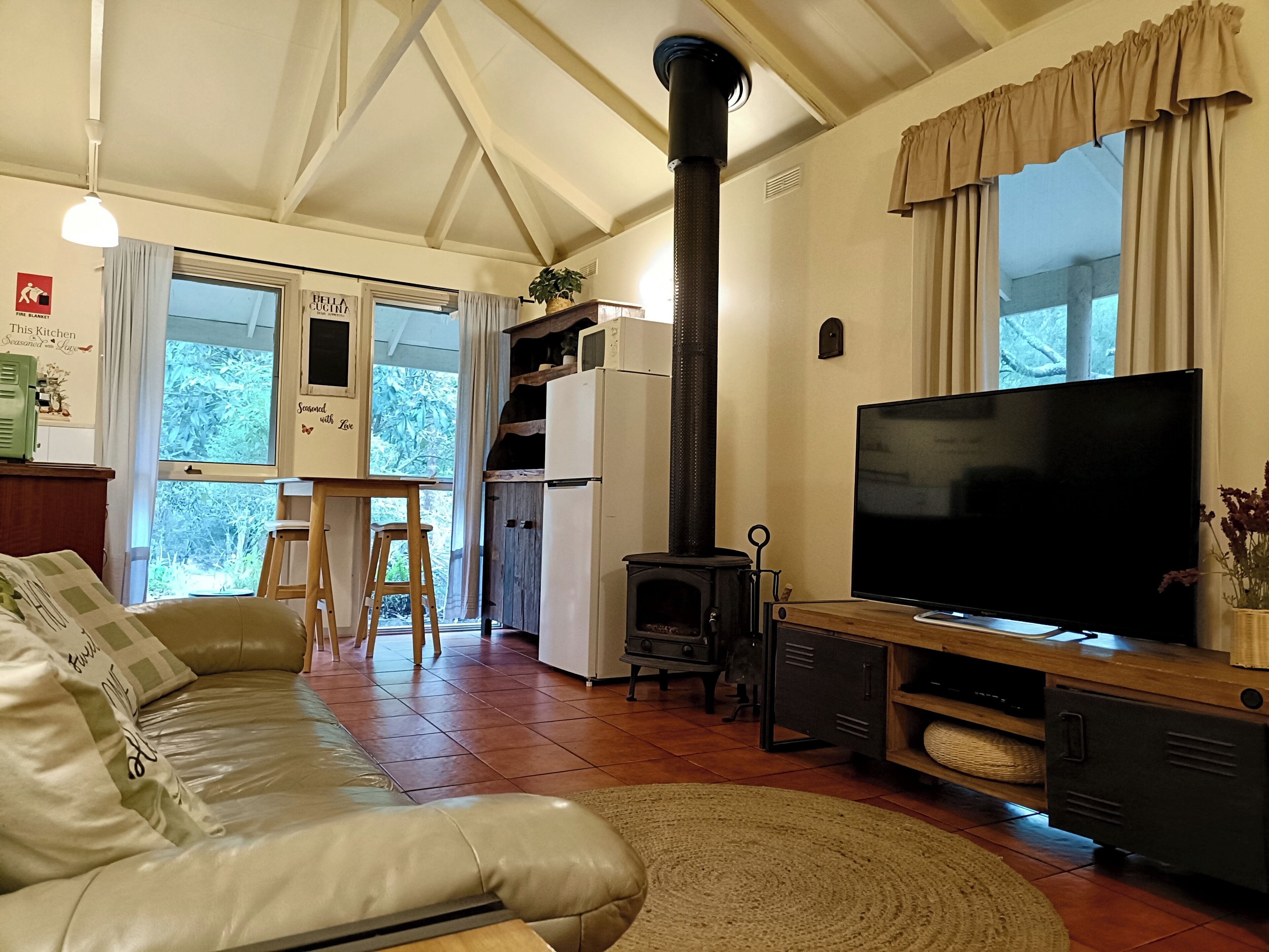 A cozy living room with a sofa, a television, a fireplace, and a kitchen area visible through an open door.