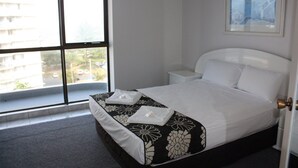 Habitación de hotel con un ventanal grande, una cama con colcha estampada, cabecera blanca y una mesita de noche con lámpara.