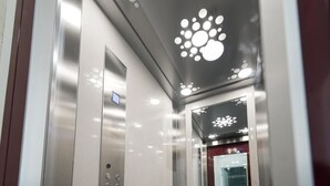 An elevator interior with a metallic finish, a digital display, and a ceiling with a geometric light fixture. - Lily Sands Inn (South Melbourne)
