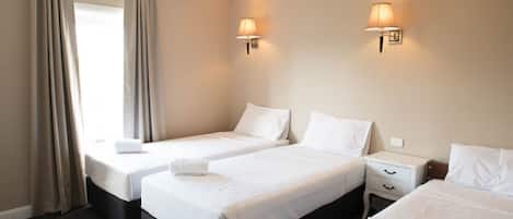 Habitación de hotel con dos camas individuales, una mesita de noche, una lámpara y una ventana con cortinas.