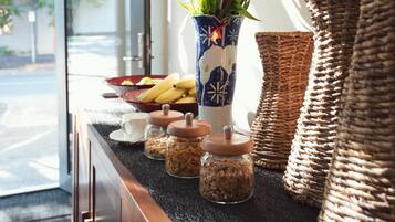 A breakfast bar with a bowl of fruit, a vase with flowers, and jars of granola.