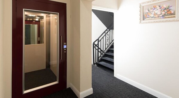 An elevator with a digital display, a staircase with a black railing, and a framed floral artwork on the wall.
