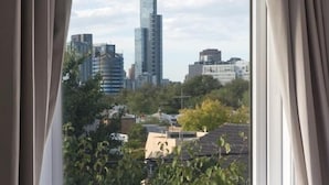 A hotel room with a large window, a bed, and a view of a cityscape including a tall building. - Lily Sands Inn (South Melbourne)