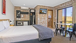 Habitación de hotel con cama, escritorio, silla, televisor y balcón con vistas.
